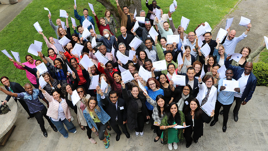 A group of people, standing outside, wave certificates in the air, celebrating the end of training.