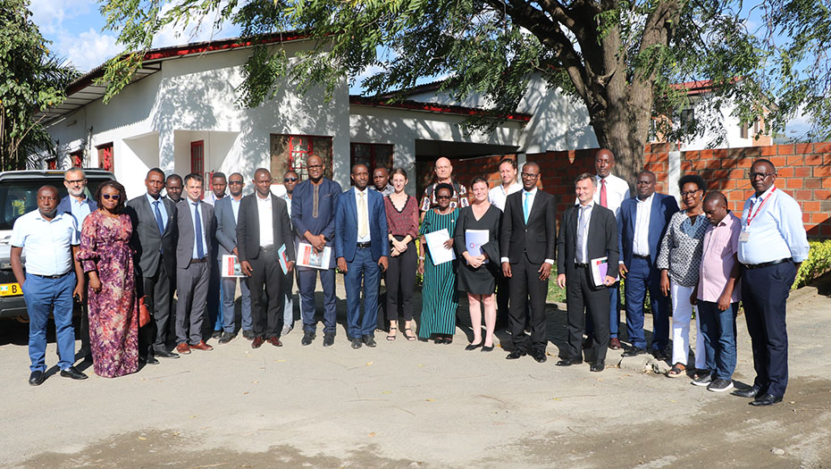 A group of people pose for an outdoor group photo in front of a white and brick building, during the launch ceremony of the 