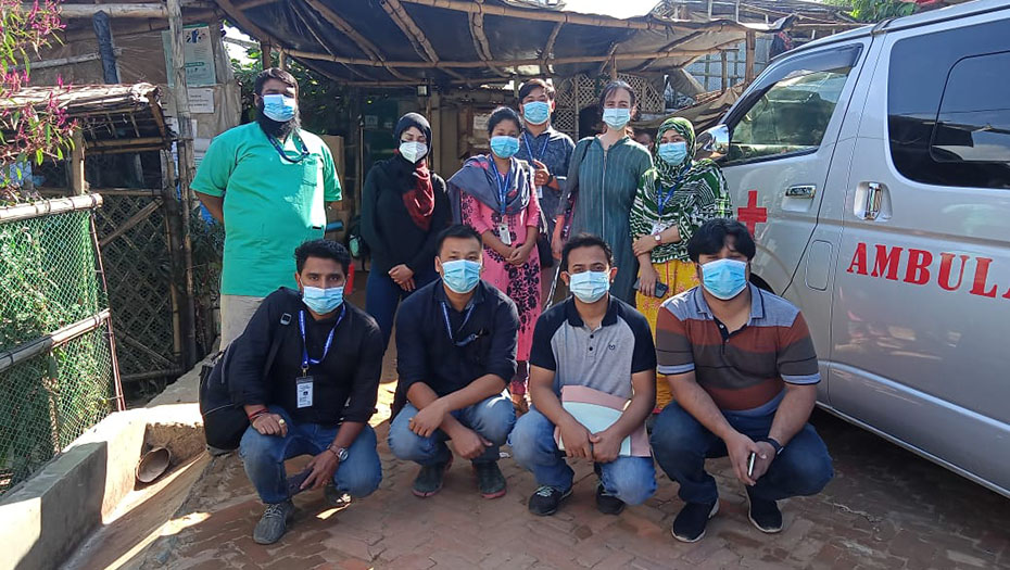 A group of people wearing masks pose next to an ambulance as part of a project to combat COVID-19.