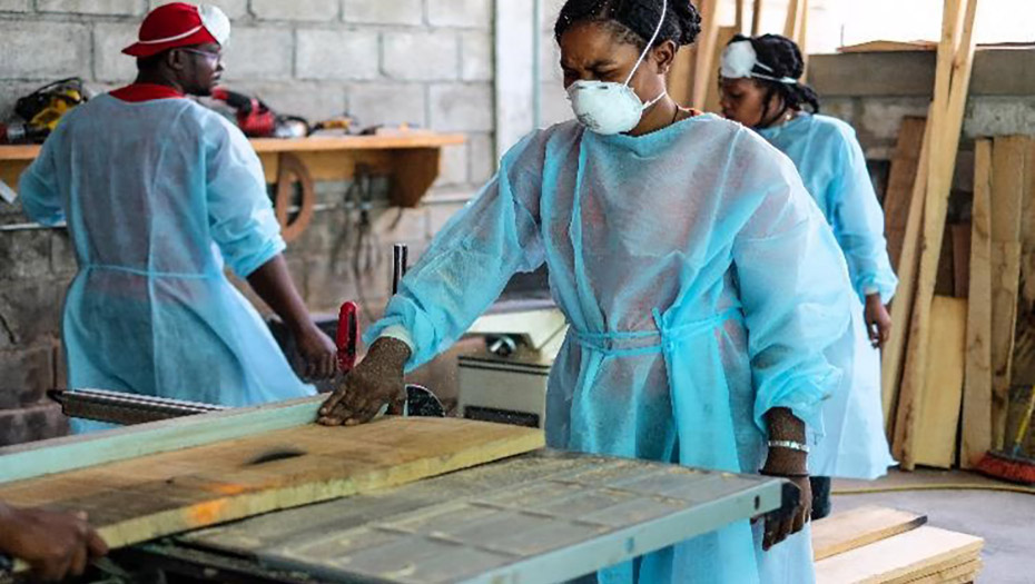 People wearing personal protective equipment, using woodworking machinery in a workshop at the GHESKIO center.