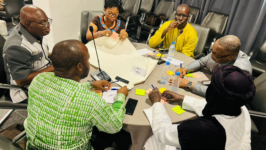 A group of people discuss around a table during a workshop, using post-it notes and papers.