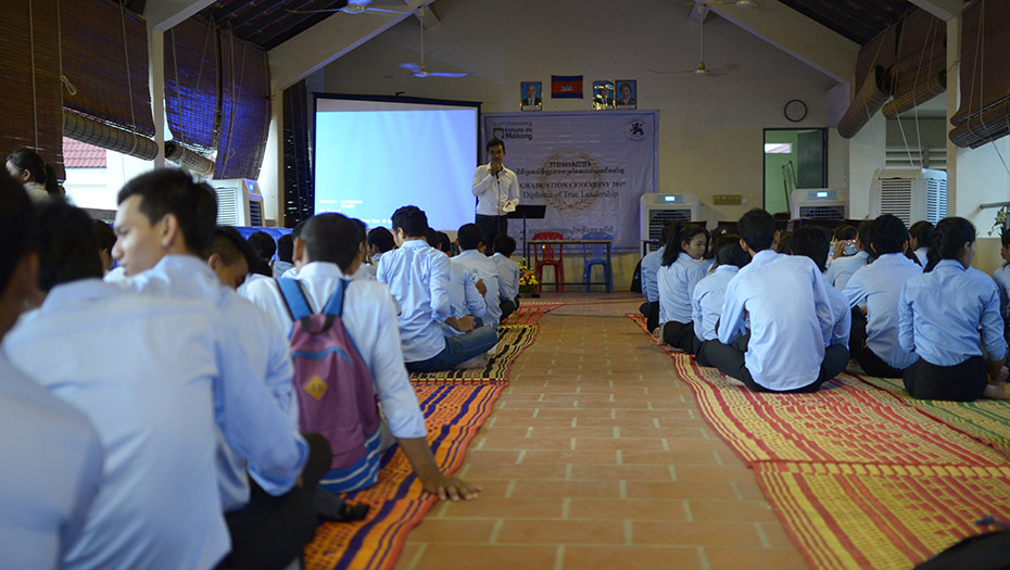 A group seated in rows on the floor, listening to a presentation in front of a projection screen.