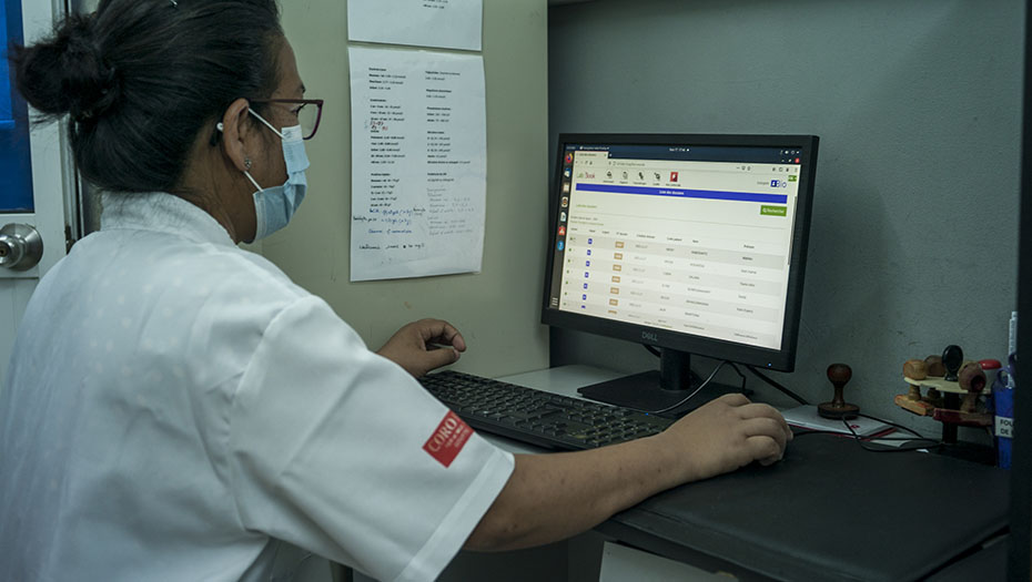 A healthcare professional using a computer in a medical laboratory, wearing a mask and gown.