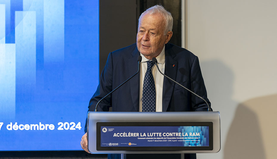 Alain Mérieux standing behind a podium labeled Accélérer la lutte contre la ram, in front of a blue screen displaying 7 décembre 2024” 