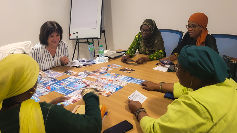 Cinq personnes assises autour d’une table de réunion, manipulant des brochures et documents imprimés avec un tableau de conférence en arrière-plan.