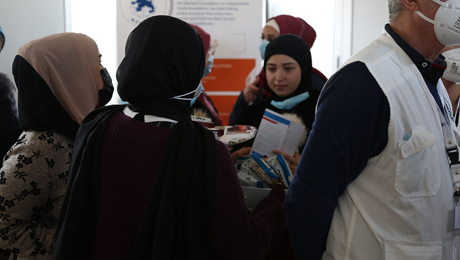 Groupe de personnes dans un centre de santé, dont une portant un gilet blanc avec badge, en intérieur avec panneau d’information en arrière-plan.