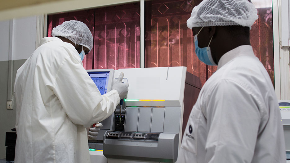 Two people in white lab coats use equipment to analyze samples related to acute respiratory infections.