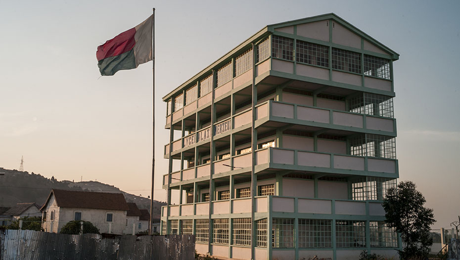 Bâtiment à plusieurs étages vert et blanc avec grandes fenêtres et drapeau rouge, blanc et vert devant l’Université Saint Vincent de Paul-Akamasoa.