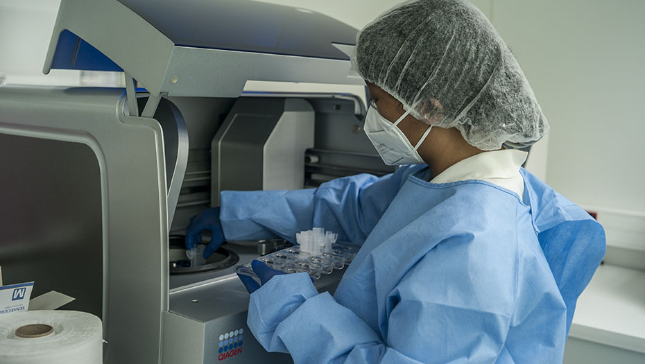 Person wearing protective gear handling test tubes in a laboratory analyzer