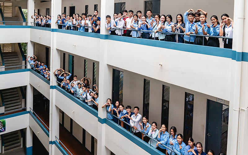 Students in uniforms standing on multi‑level balconies of a school building facing the camera.