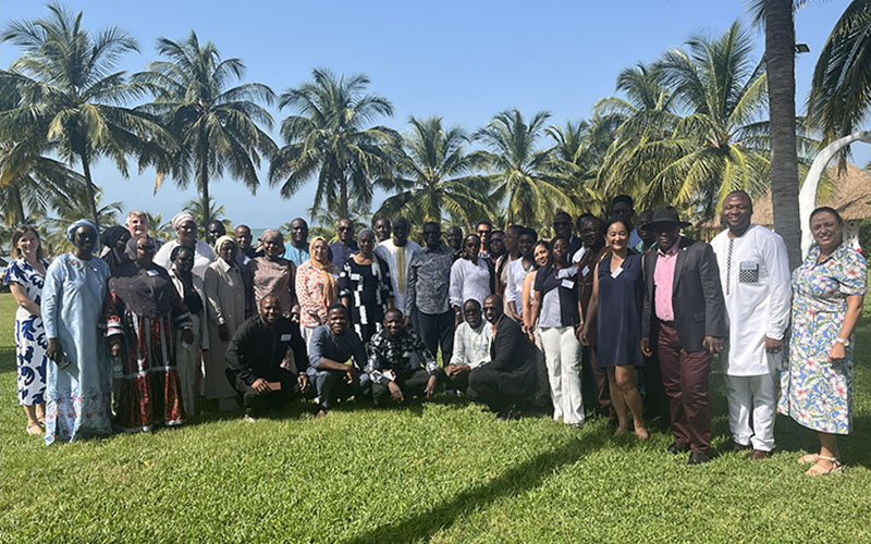 Large group of participants posing on a lawn with palm trees in the background.