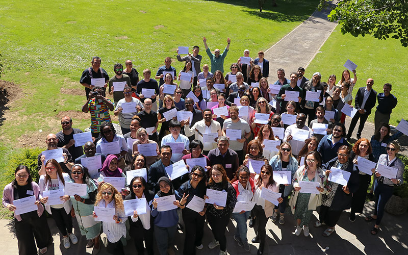Large group of participants holding certificates and raising their arms on an outdoor lawn.