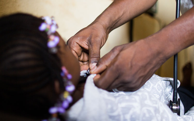 Health worker handling a medical device on a child lying down during an examination.
