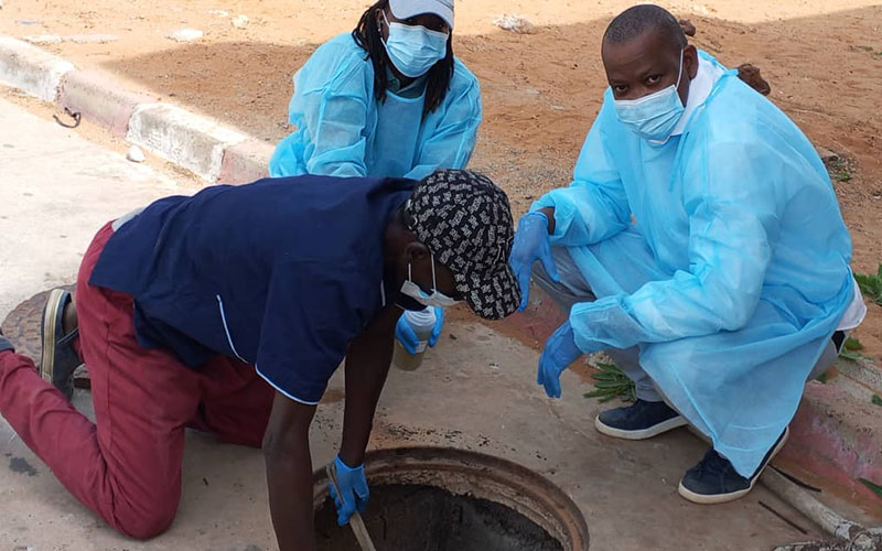 Three individuals wearing protective gear inspecting a manhole in the field.