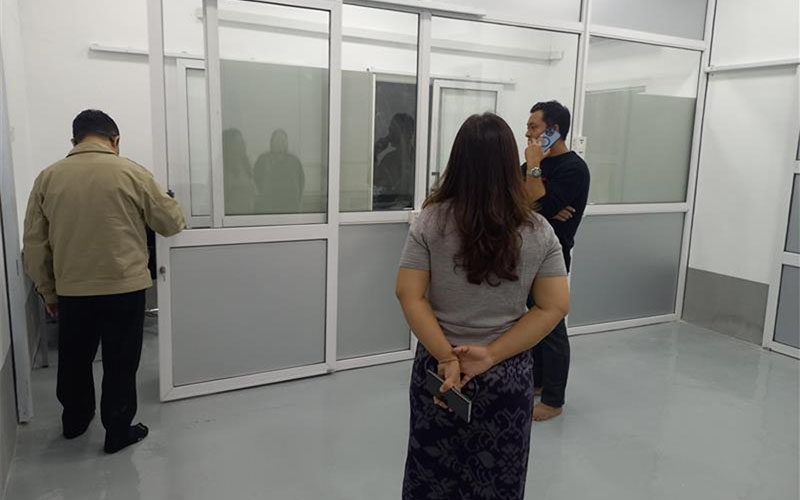 Three individuals standing in a laboratory with glass partitions observing workspaces.
