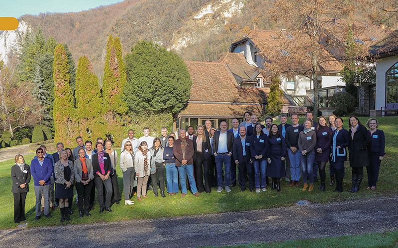 Group of participants posing in front of a tiled-roof building with trees in the background.