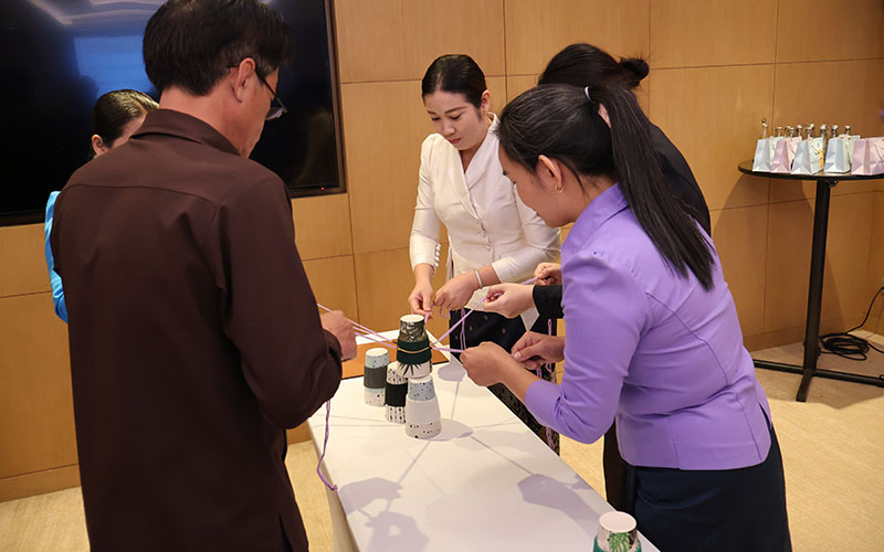 Several people around a table assemble a structure using strings and cups during a group exercise.