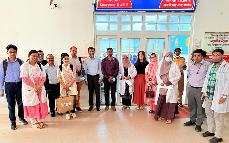 Group of people posing in front of a hospital department entrance with a Pediatric Emergency & AMU sign above them.