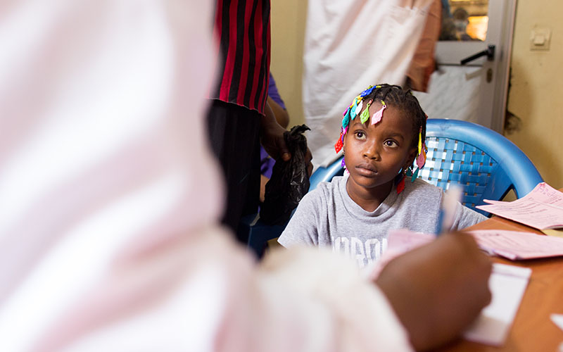 Child sitting and looking at an adult in front of a table with documents in a health center.